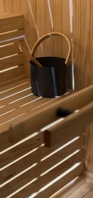 Wood-lined sauna bench with a bucket and ladle, light falling through the slats