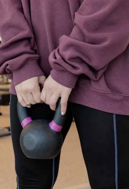 A member in a plum sweatshirt holds a kettlebell